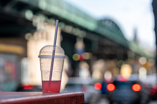Germany, Berlin, March 17, 2024 - Clear plastic cup with a drinking straw against street at city, Berlin Prenzlauer Berg