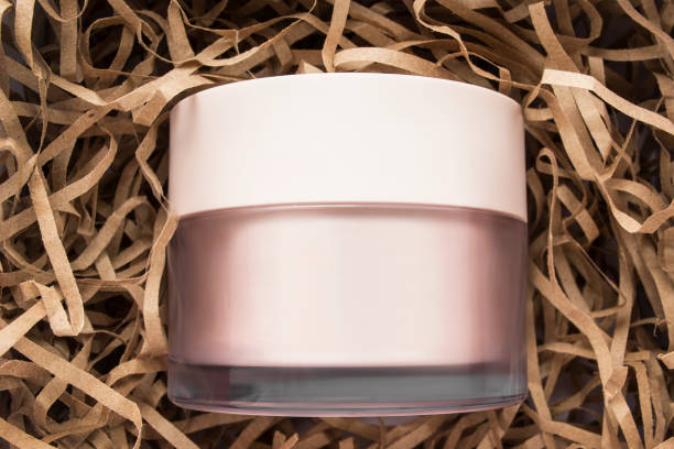 Blank beige cosmetic cream jar lying in brown shred packaging paper