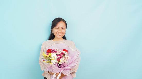 Happy woman holding vibrant bouquet of flowers on light blue background