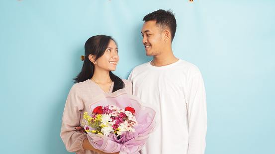 Happy couple sharing a moment with a colorful bouquet on a soft blue background, exuding love and joy