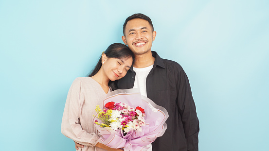 Joyful man and woman with fresh flowers, enjoying a light-hearted moment against a cyan backdrop