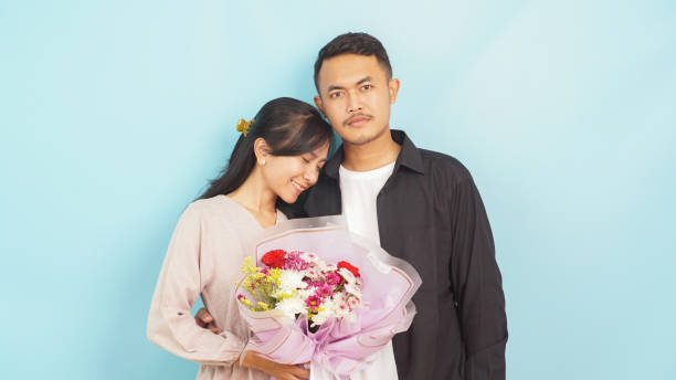 Loving pair exchanging glances with a beautiful bouquet, celebrating togetherness against a blue background