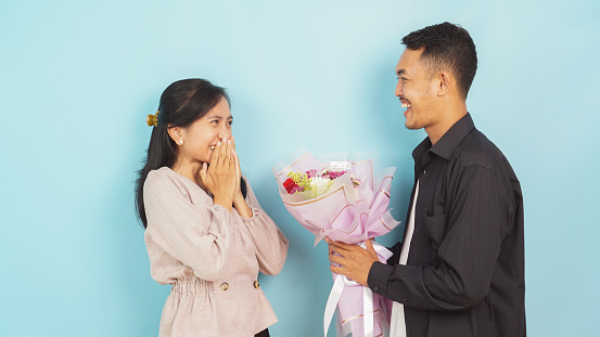 Delighted woman receiving a bouquet from a man, expressing surprise and joy on a blue background