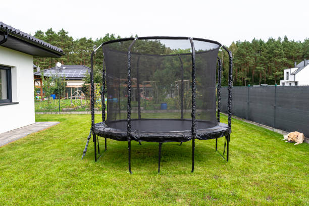 istock Large childrens jumping trampoline with protective net and closed zipper, standing in the garden, visible golden retriever dog. 2147511527