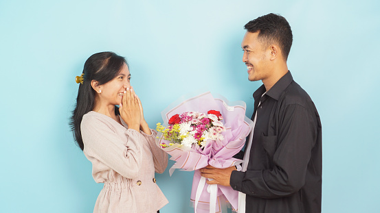 Delighted woman receiving a bouquet from a man, expressing surprise and joy on a blue background