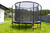 Large childrens jumping trampoline with protective net and closed zipper, standing in the garden, visible golden retriever dog.