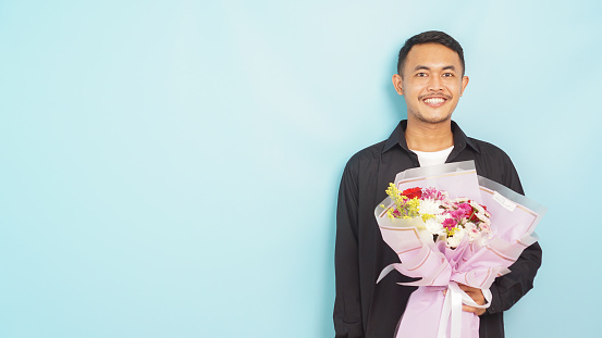 Man with a beaming smile presenting a fresh bouquet, embodying a gesture of love on a tranquil blue background