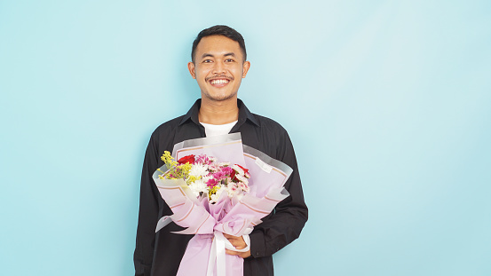 Man with a beaming smile presents a fresh bouquet, embodying a gesture of love on a tranquil blue background