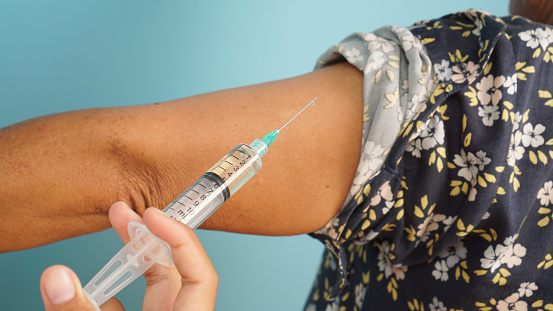 Healthcare administration in action, with a close-up of a vaccine injection into a patient’s arm, against a pastel blue background