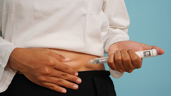 Patient self-administering insulin injection in the abdominal area for diabetes management on a blue background