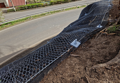 reinforcing slope with steel net anchored deep into rock. falling loose rock stones do not fall on road. anchored with steel nails with nuts. drilled into subsoil and fasten the mesh, train track, land slide, rock face, edge