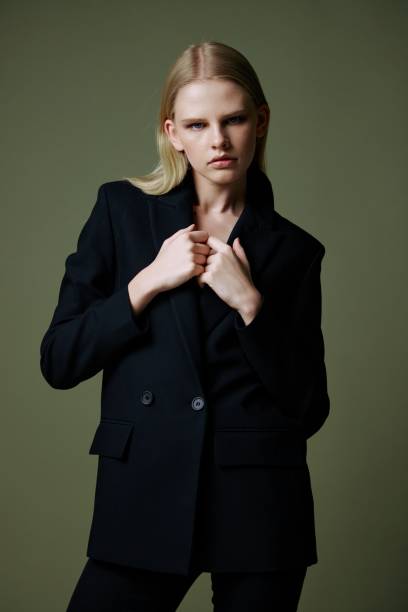 istock The model holds the jacket by the collar while posing on a green background in the studio. Concept photo for clothing brands. Cool offer for fashionable suits 2147513731