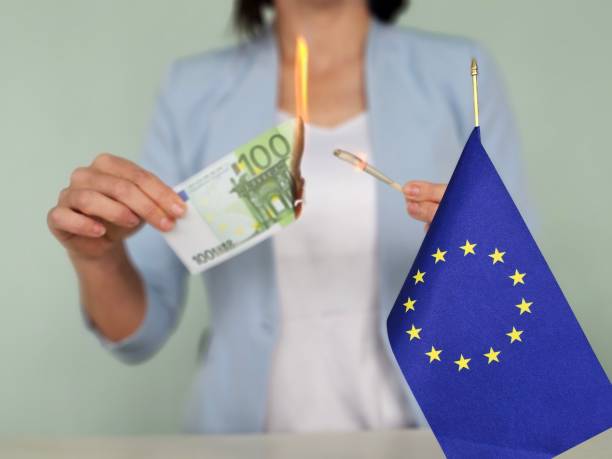 istock Burning euro banknotes in hands and flag 2147514732