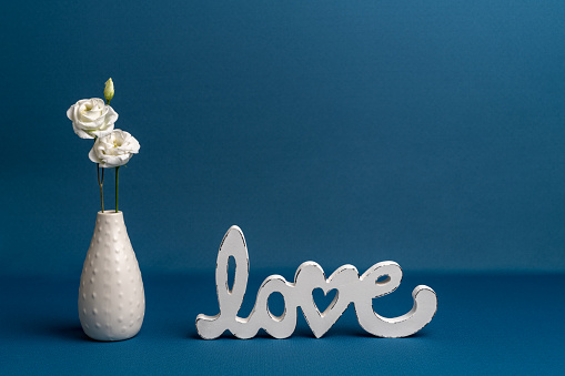 White small roses in a white vase on a blue background next to the white inscription \