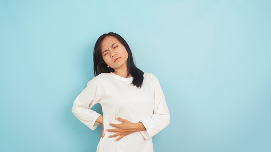 Woman enduring menstrual back pain, dressed casually against a calm blue backdrop, conveying discomfort and the need for relief