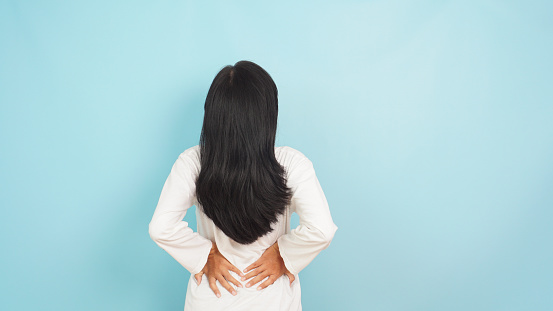Asian woman backache, lower backpain due to menstruation on light blue background