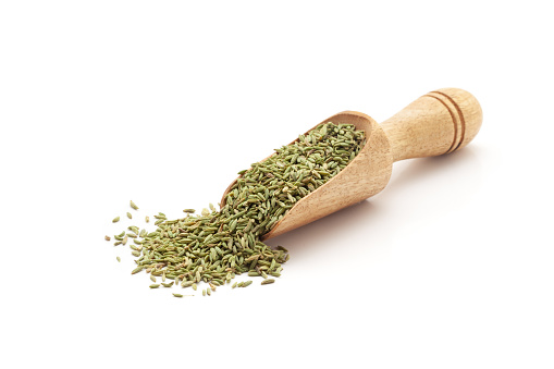 Front view of a wooden scoop filled with Organic Small Fennel Seeds (Foeniculum vulgare). Isolated on a white background.