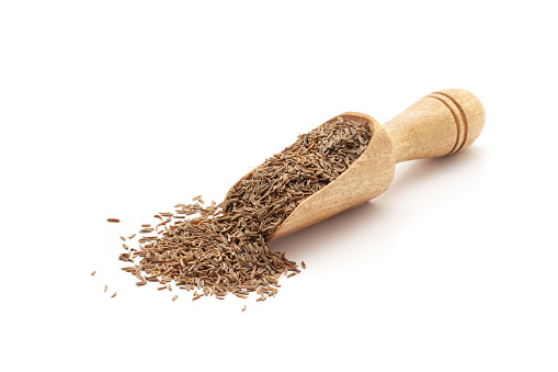 Front view of a wooden scoop filled with Organic Caraway seeds (Carum carvi). Isolated on a white background.