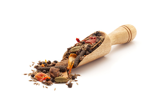 Front view of a wooden scoop filled with Organic warming spices or whole Garam Masala. Isolated on a white background.
