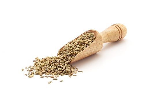 Front view of a wooden scoop filled with Organic Fennel Seeds (Foeniculum vulgare) Badi saunf. Isolated on a white background.