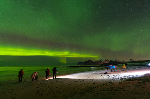 Photographers on a beach admiring northern lights in the starry night sky, Storsandnes, Lofoten Islands, Norway