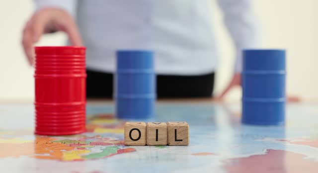 Woman places toy barrels of liquid near word Oil on table