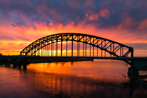 Oude IJsselbrug bridge in an amazing colorful sunset over the river IJssel in Overijssel, Netherlands during springtime seen from above. The strong colors in the sky are partly caused by the southern wind bringin sand from the Sahara desert over the European contintent.