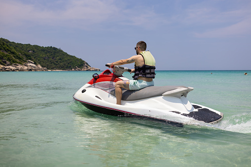 Man enjoying a thrilling ride on a jet boat on turquoise waters of a tropical beach at Ko Phangan Island, Thailand.
