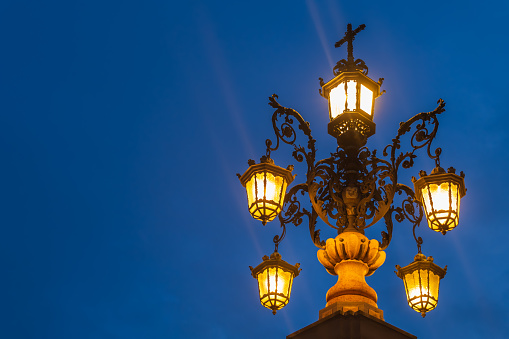 Ornate lamp post of Fuente de la Farola fountain illuminated at night, isolated against evening sky in Seville, Andalusia, Spain.