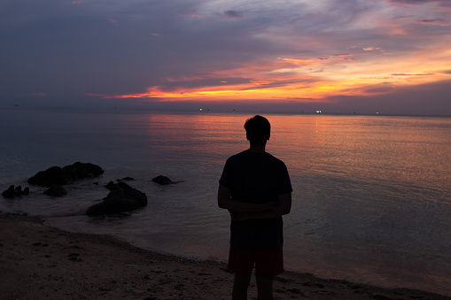 Contemplation at the beautiful sunset. Silhouette of the young man on the beach.