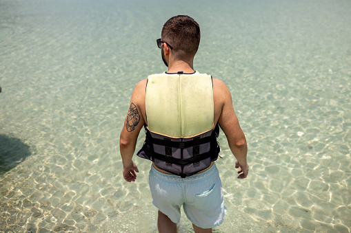 Man in life jacket standing in the shallow sea at the tropical beach at Ko Phangan Island, Thailand.