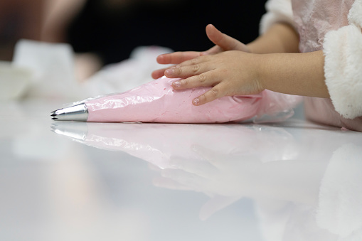 Tiny hands shape a bag of pink whipped cream on a white table