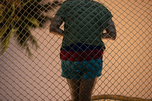 Unrecognizable man leaning on chain-link fence at Ko Phangan Island, Thailand.