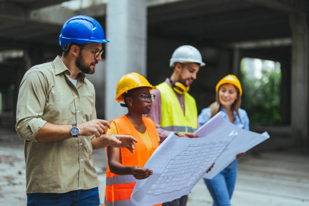 istock Group of civil engineers looking at blueprints at a construction site and wearing helmets. 2147522649