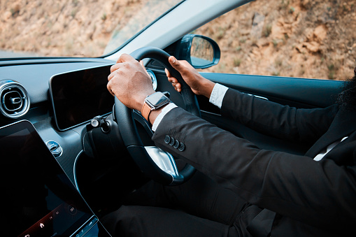 A well-dressed businessman with a smartwatch drives a modern luxury car, symbolizing success, mobility, and high-end lifestyle. The focus on the steering wheel highlights control and determination.