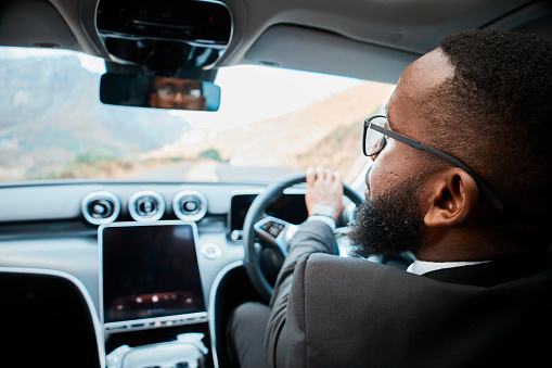 Rear view of a focused African American businessman driving a luxury car. Well-dressed male in glasses takes the wheel confidently, embodying success and lifestyle.