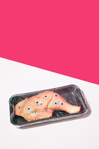 Chicken with googly eyes, wrapped in plastic packaging giant white pink background. Surrealism. Creative and humorous food presentation. Concept of food pop art photography, creativity, quirky style