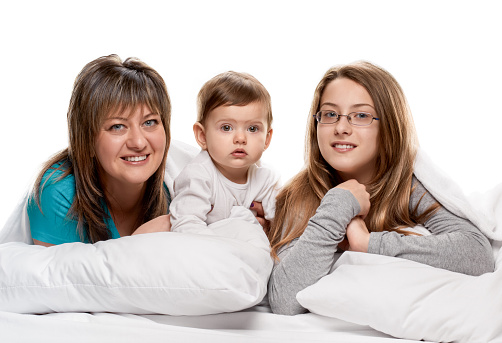 Portrait of a mother with her teenager and little daughters in the bed on white background
