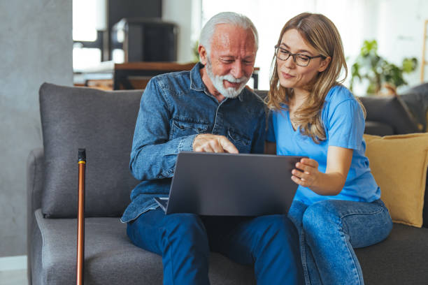 istock Active senior man using laptop with female carer sitting by on sofa at home. 2147526385