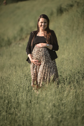 A young pregnant woman enjoying nature, embracing her belly and smiling.