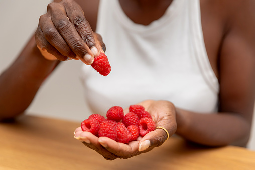 close up of Woman Holding Raspberries in One Hand and Picking One with Other