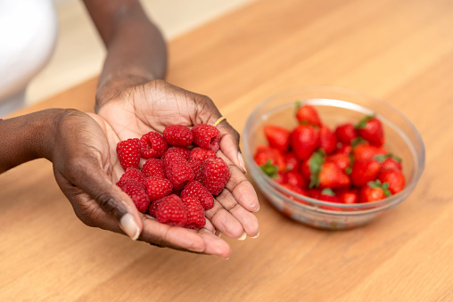 close up of Handful of Ripe Raspberries and a Glass Bowl with strawberries in the Background