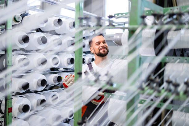istock Experienced textile factory worker changing thread spool on industrial knitting machine. 2147529228