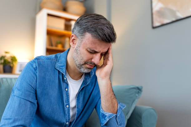istock Closeup of man suffering from headache at home, touching his temples, copy space, blurred background. Migraine, headache, stress, tension problem, hangover concept 2147529436