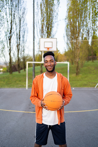 Vertical portrait of a smiling afro young man in a basketball court