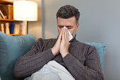 Man feeling sick lying in the bed having flue. Sick man lying on sofa checking his temperature under a blanket at home in the living room