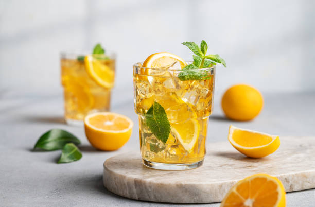 Two glasses with iced drink with lemon and mint on a marble board on a light background with shadow and citrus fruits. Two glasses with iced drink with lemon and mint on a marble board on a light background with shadow and citrus fruits. The concept of a cold tea or lemonade on a hot summer day. Front view. carbonated juice stock pictures, royalty-free photos & images