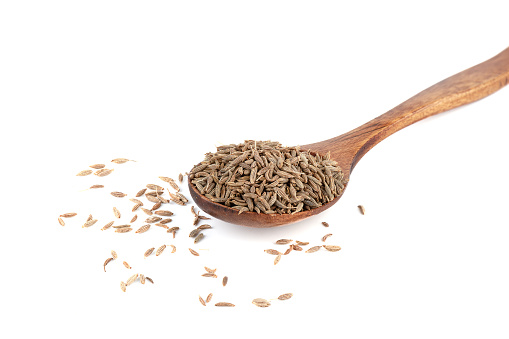 Dried cumin seeds on wooden spoon on white background. Seasoning for food.