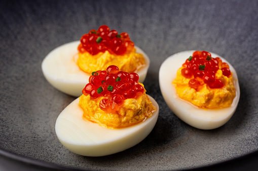 Deviled egg with salmon caviar on a grey plate.