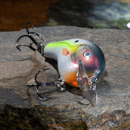 Colorful fishing lure on a rock next to a lake's water